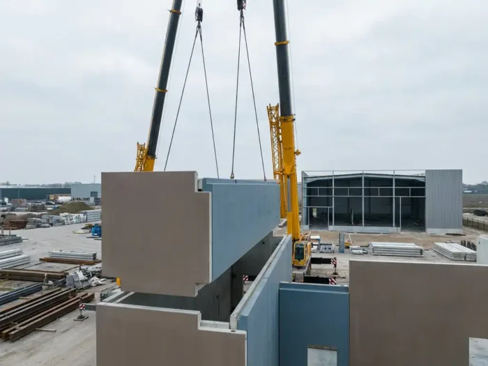 Modulaire geprefabriceerde bouwsectie wordt door kraan geplaatst op industrieterrein met gedeeltelijk gebouwde loods