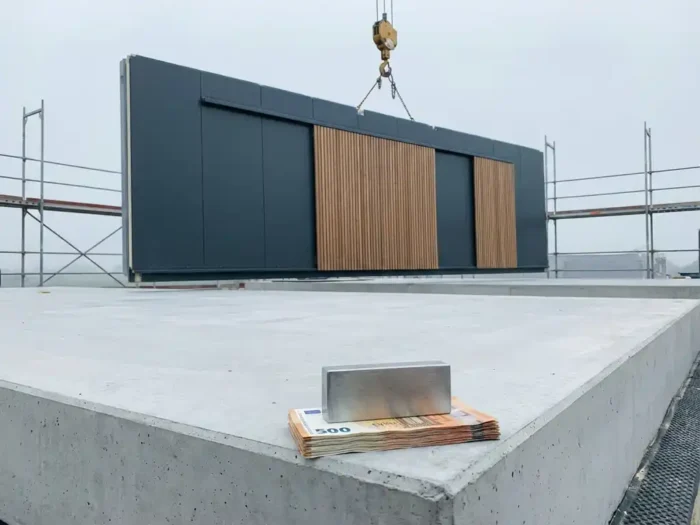 Prefab wandpaneel wordt door kraan op betonnen fundering geplaatst, eurobiljetten onder presse-papier op moderne bouwplaats